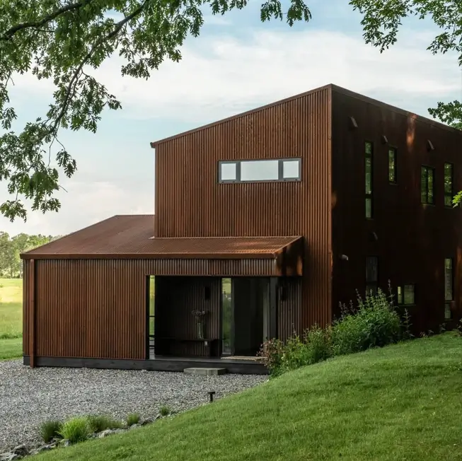 37 Brown House with Black Trim Ideas for a Warm, Modern Exterior 4 Rust-brown corrugated steel barn-style home with a charcoal ribbon window and shadowed dark entry in an open field