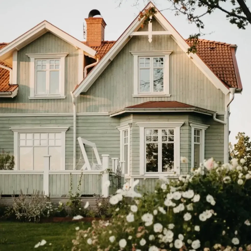 43 Green House With White Trim Ideas for Fresh Curb Appeal 4 pale green house with white trim, deep window casings, and terracotta tile roof on a Swedish-style cottage