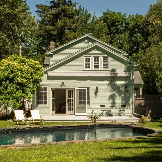 43 Green House With White Trim Ideas for Fresh Curb Appeal 5 sage green house with white trim, French doors, and awning on a farmhouse rear exterior with a pool