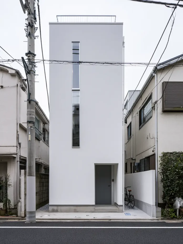 Modern Japanese House Design: 58 Ideas, Costs, and What Defines the Style 32 A very narrow white render house with a single tall slot window and a rooftop railing.