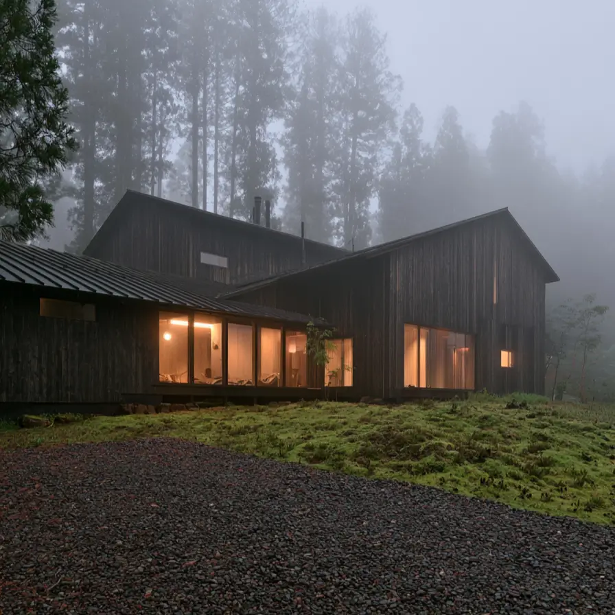 Modern Japanese House Design: 58 Ideas, Costs, and What Defines the Style 50 Charred timber gables under a shallow metal roof, half lost in fog with warm light in the windows.