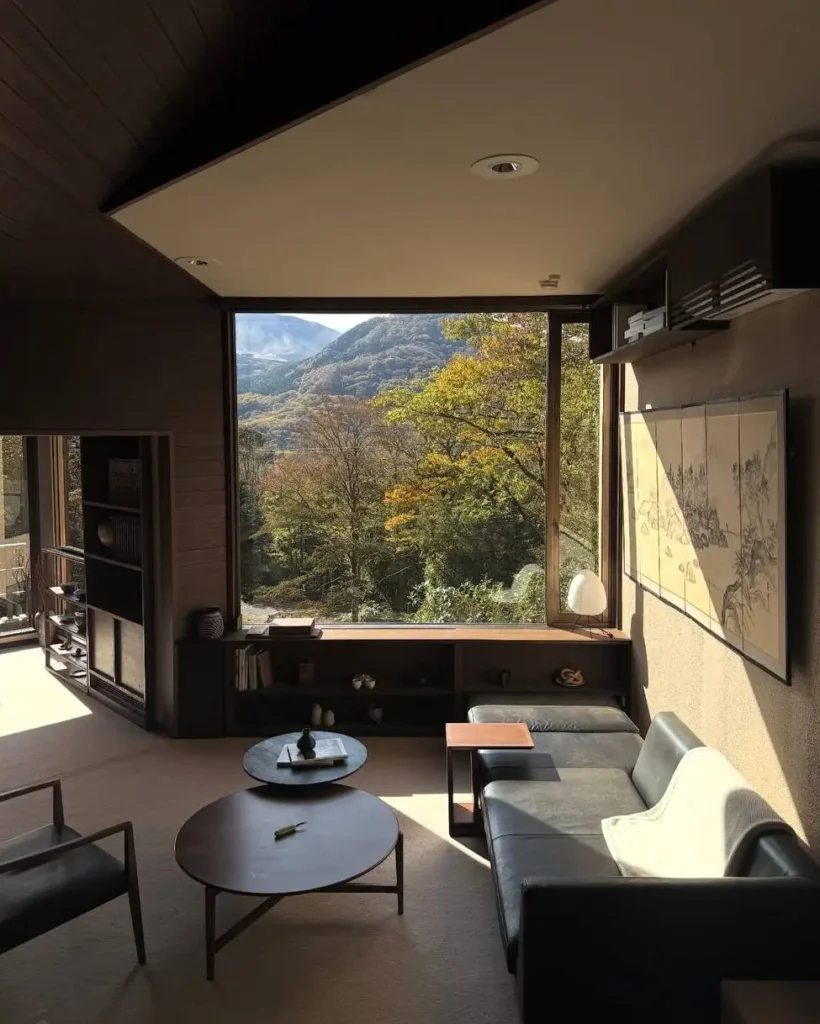 Modern Japanese House Design: 58 Ideas, Costs, and What Defines the Style 54 A living room in a modern Japanese house with a wide mountain-view window above built-in low timber storage.