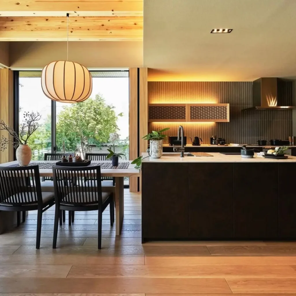 Modern Japanese House Design: 58 Ideas, Costs, and What Defines the Style 59 A modern Japanese house kitchen with a dark stone island beside a low oak dining table and full-height garden glazing.