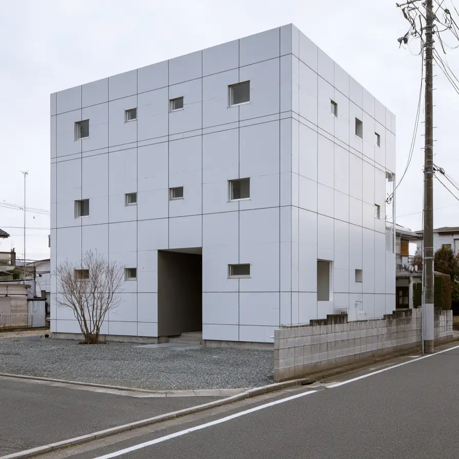 Modern Japanese House Design: 58 Ideas, Costs, and What Defines the Style 9 Pale cladding panels set in a visible grid with scattered small square windows and a recessed entrance void.