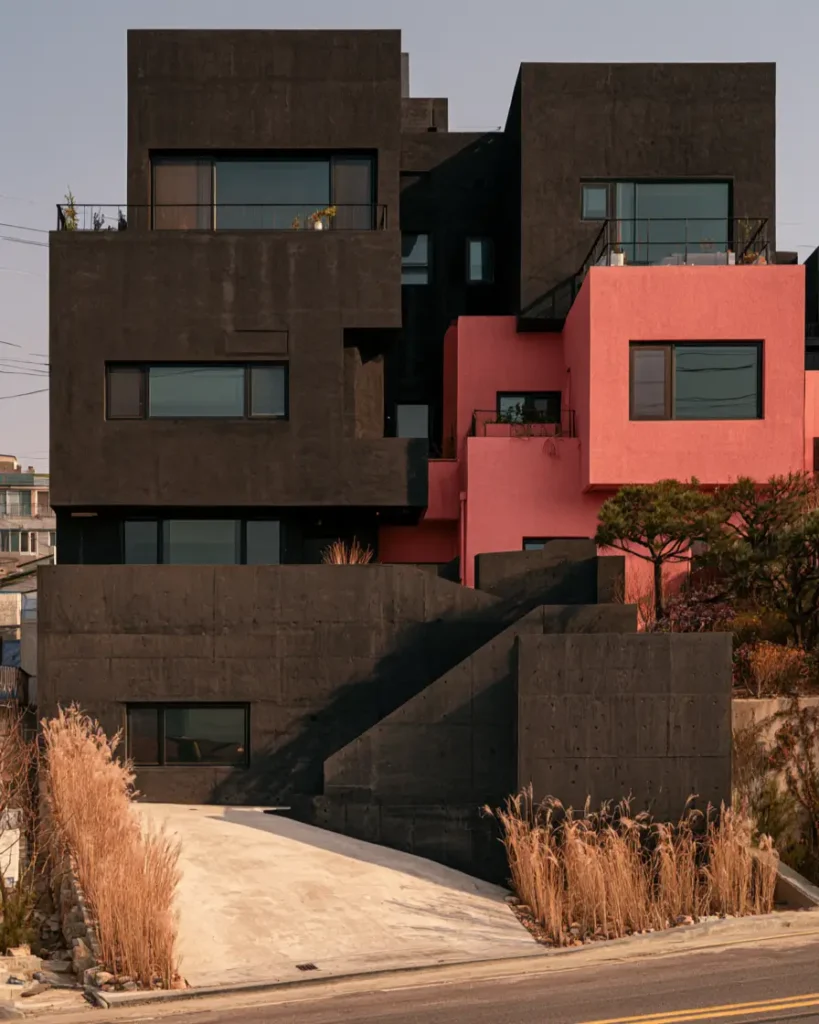 26 Black and Pink Houses Worth Saving Before You Paint 12 Modern concrete hillside home with stacked charcoal volumes and one coral-pink block among the dark forms