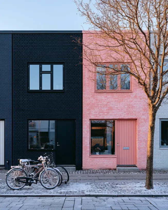 26 Black and Pink Houses Worth Saving Before You Paint 20 Painted brick townhouses side by side, one soft pink and one black, with matching windows on a cobbled street