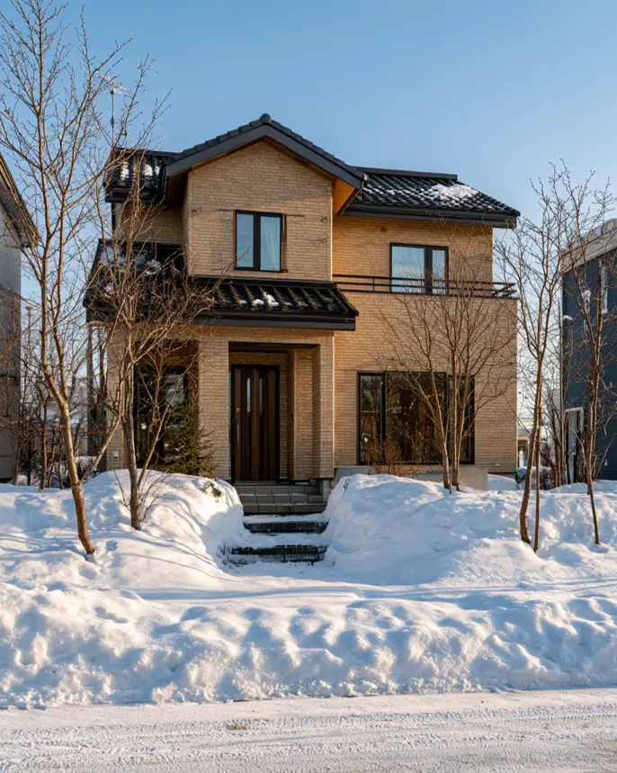 Blonde Brick House Ideas: 24 Warm Exteriors That Still Feel Fresh 22 Blonde brick house in snow with brick glowing gold in low winter sun, a wood door, black windows, and a gable roof