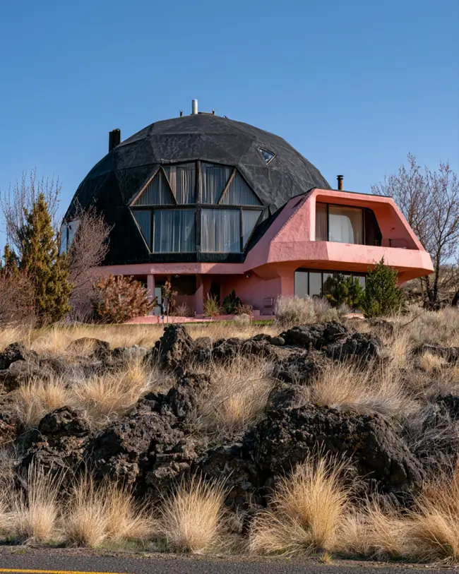 26 Black and Pink Houses Worth Saving Before You Paint 11 Geodesic dome home with a black domed shell and a curved pink concrete wing in high desert rock