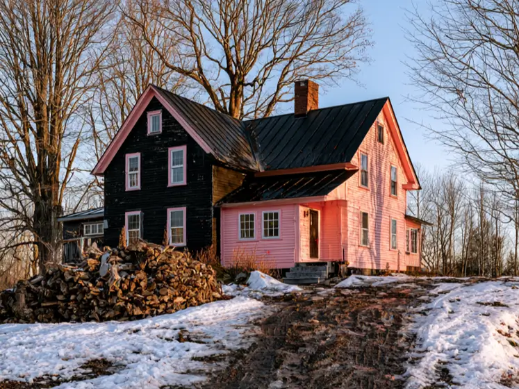 26 Black and Pink Houses Worth Saving Before You Paint 2 Black and pink houses: a two-tone farmhouse with a black clapboard wing, pink window trim, and a pink wing under a black metal roof in winter